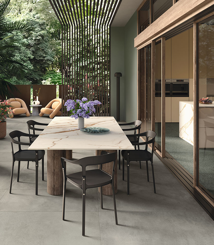 Zona pranzo outdoor contemporanea con pavimento della collezione Masterpiece effetto pietra nella tonalità Master Gray, elementi Piece Alpi e tavolo con superficie della collezione Delight effetto marmo Calacatta Oro.